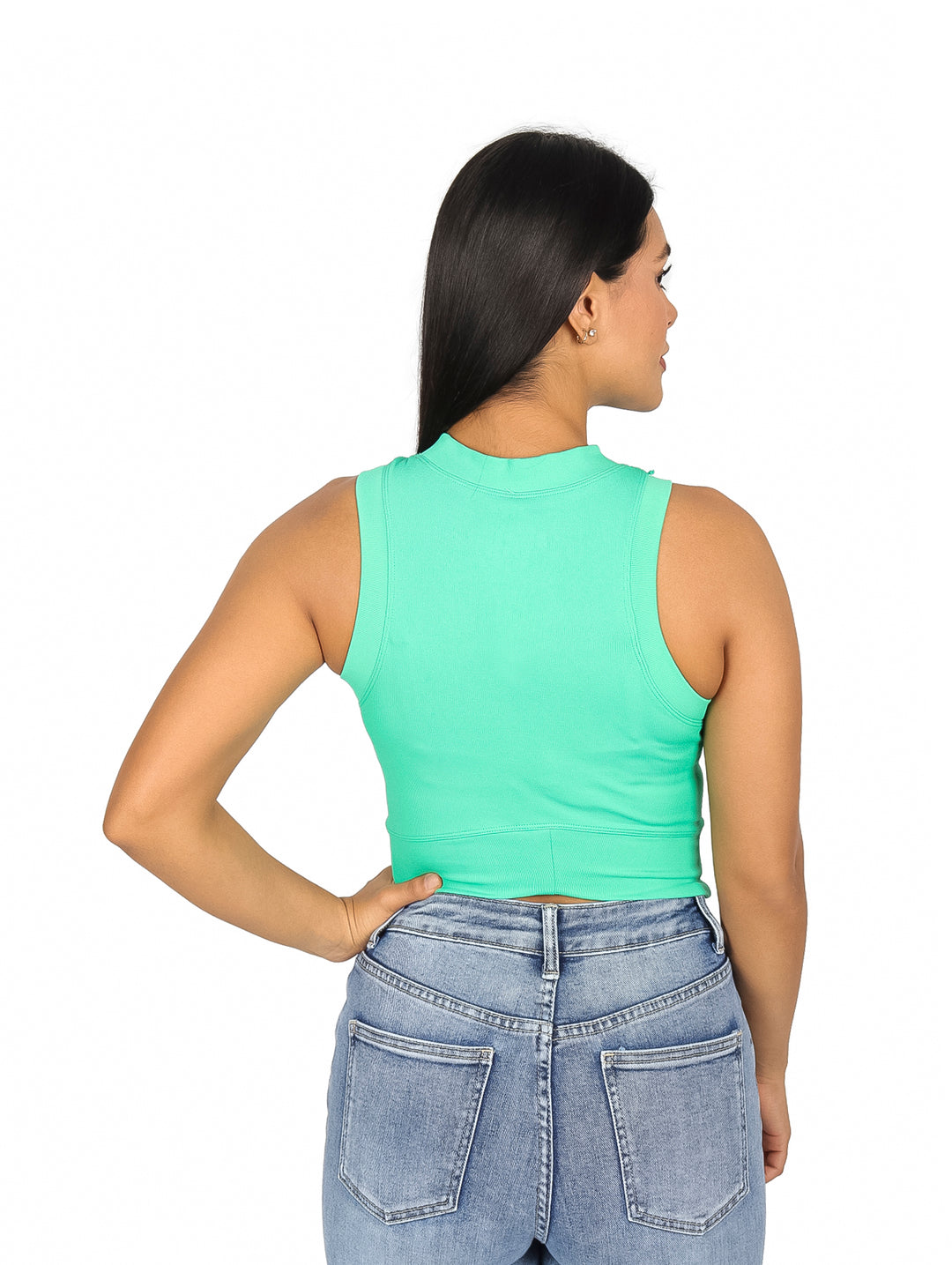 Mujer usando un top verde sin mangas y jeans azules sobre fondo blanco.