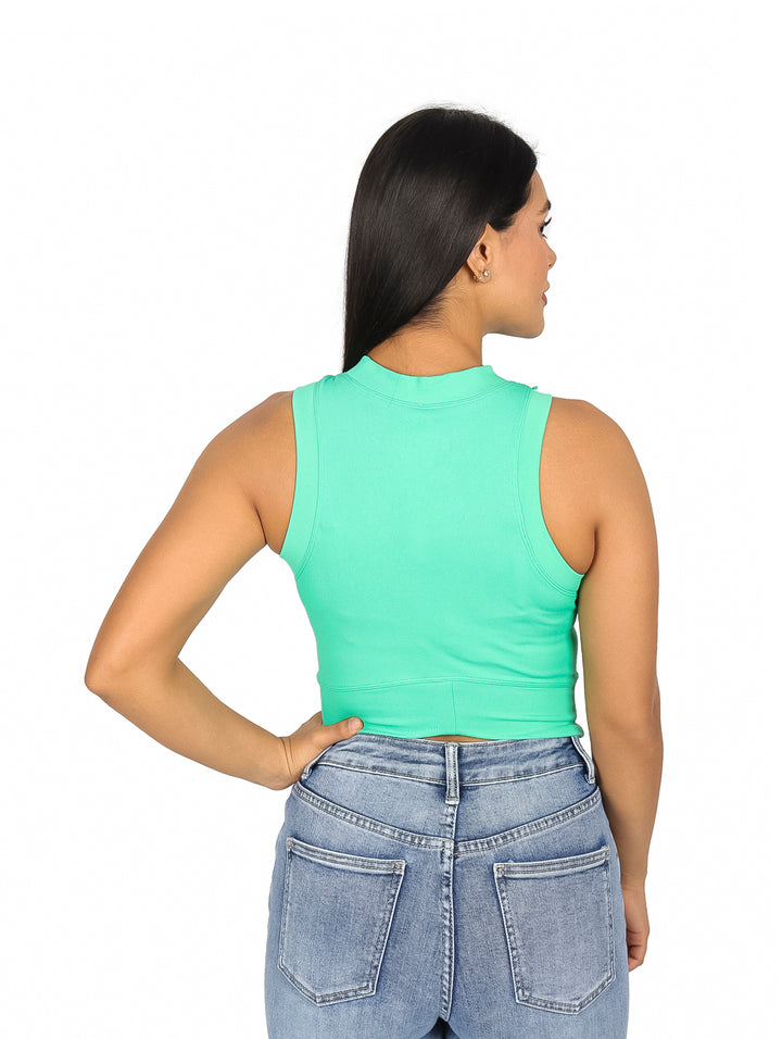 Mujer usando un top verde sin mangas y jeans azules sobre fondo blanco.
