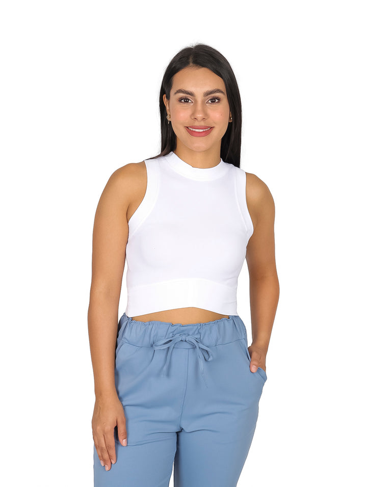 Mujer vistiendo un top blanco sin mangas y pantalones azul claro sobre fondo blanco.