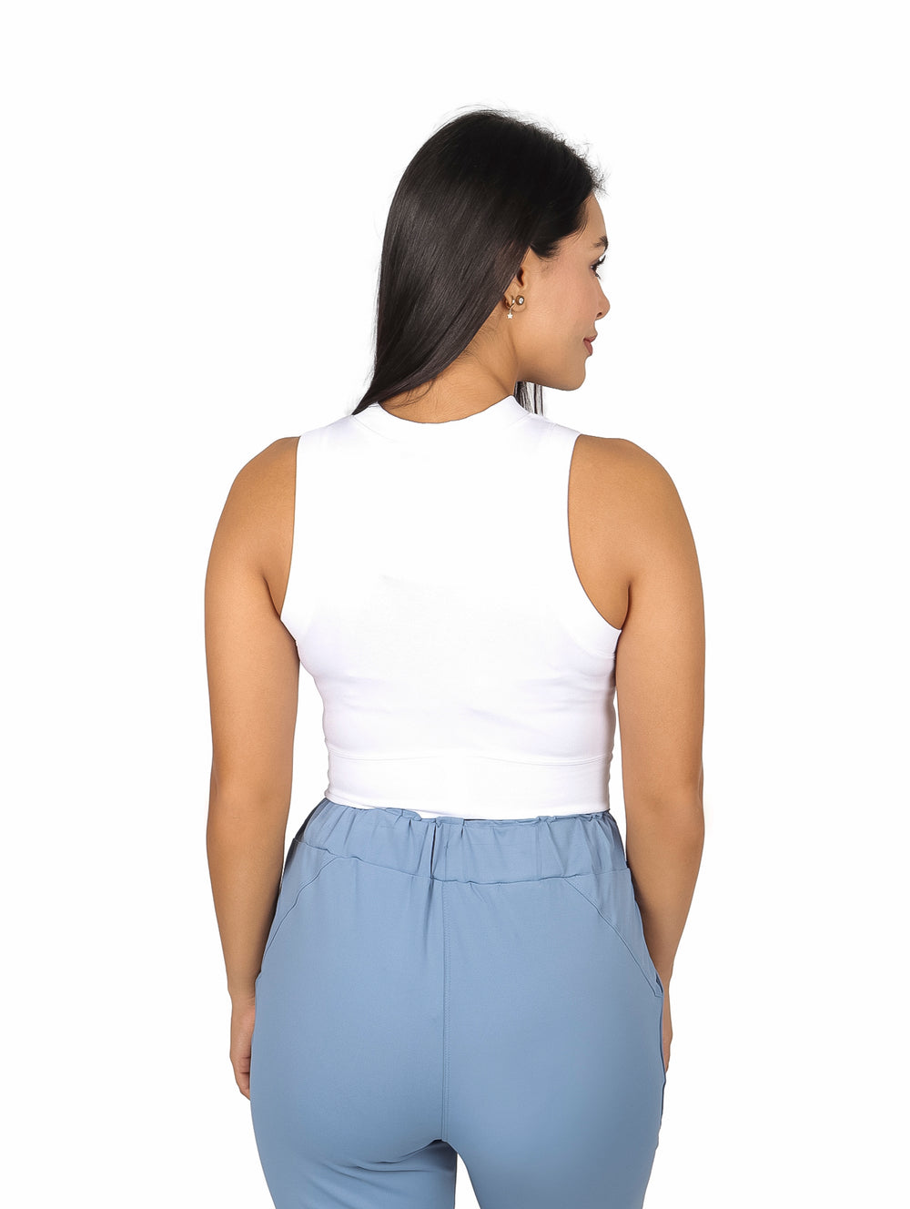 Mujer vistiendo un top blanco sin mangas y pantalones azul claro sobre fondo blanco.