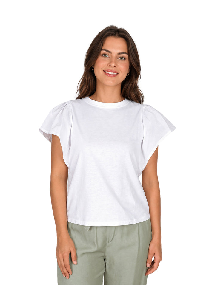Mujer vistiendo blusa blanca de manga corta con detalles de escarola y pantalones color verde claro.