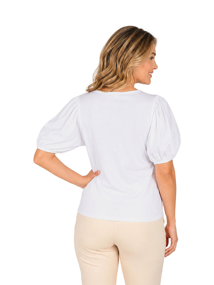 Mujer vistiendo blusa blanca con manga globo y pantalones color beige sobre fondo blanco.