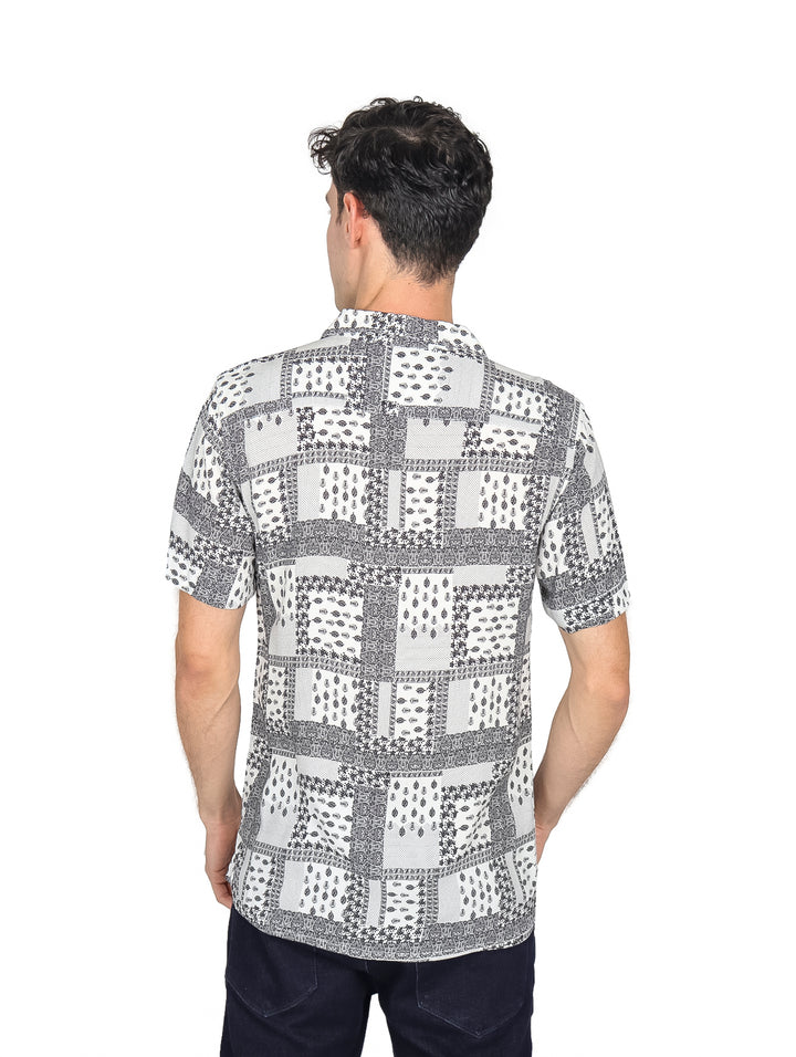 Hombre vistiendo camisa de manga corta color blanco con estampado geométrico en negro, estilo resort.