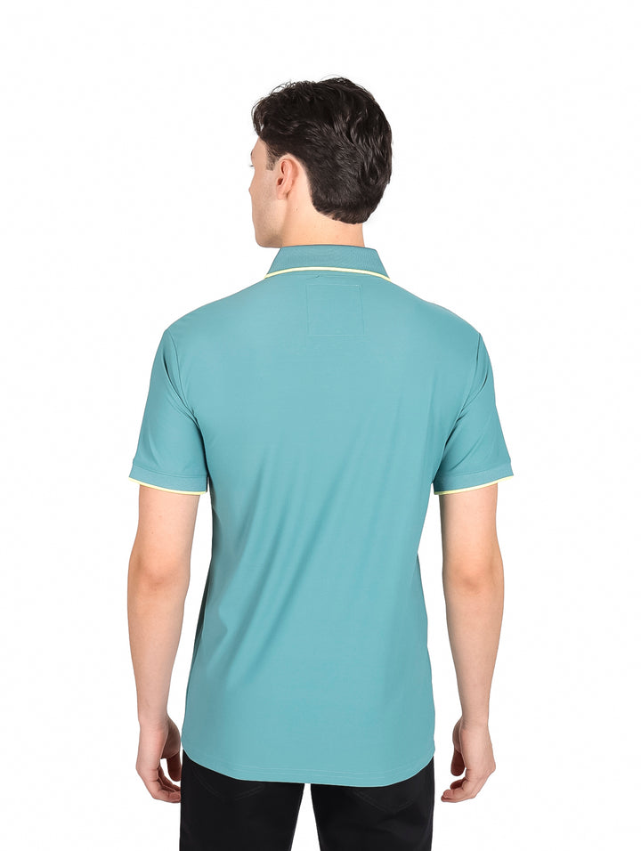 Hombre vistiendo playera polo color teal con detalles amarillos en cuello y mangas.
