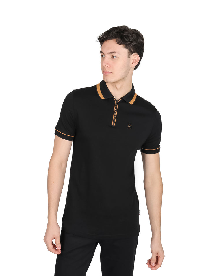 Hombre vistiendo playera polo negra con detalles en oro pálido en el cuello, cierre y mangas.