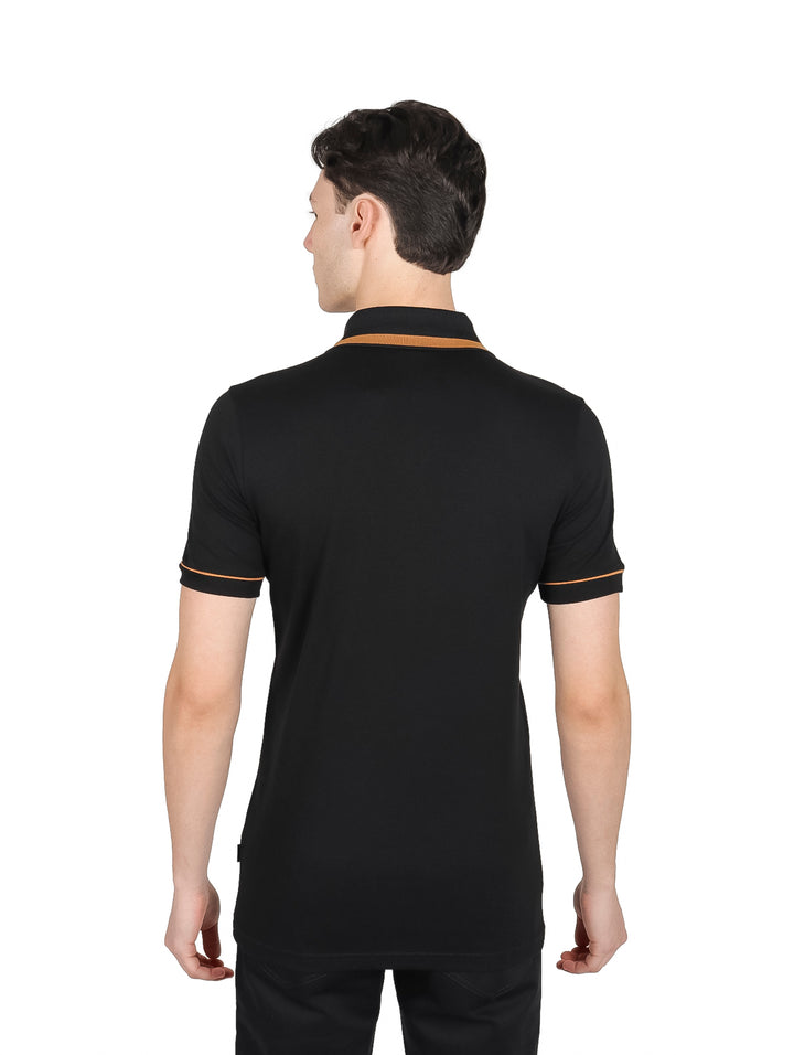 Hombre vistiendo playera polo negra con detalles en oro pálido en el cuello, cierre y mangas.
