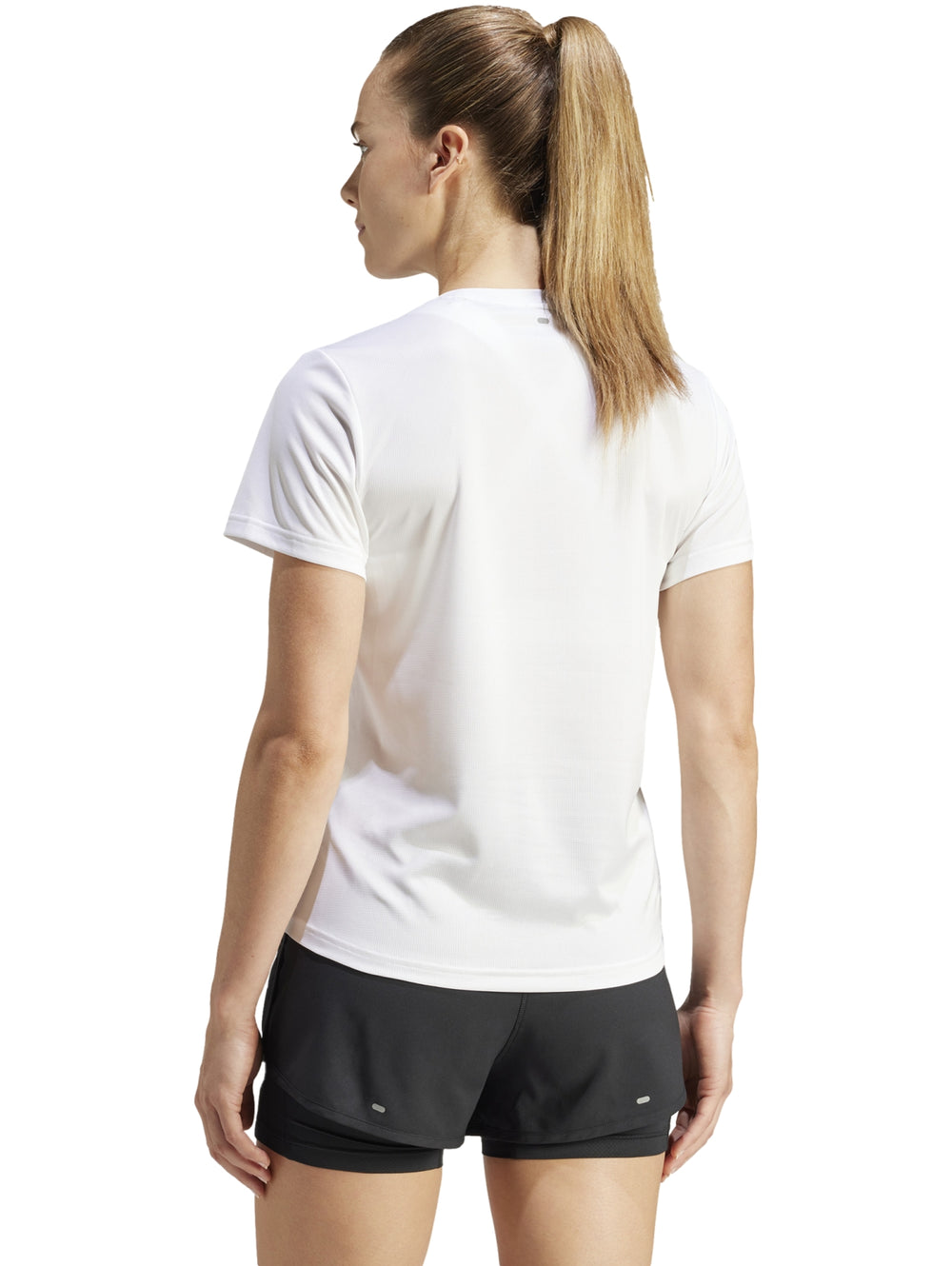 Camiseta deportiva blanca de manga corta con logo de Adidas en el pecho, modelada por una mujer.