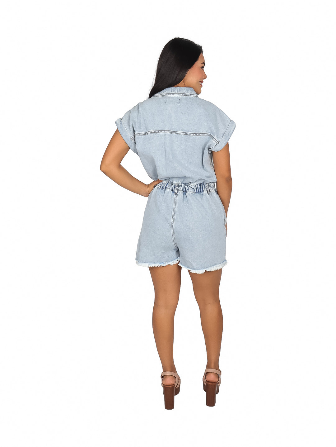 Mujer vistiendo un jumpsuit corto de mezclilla color azul claro con botones frontales y cintura elástica.