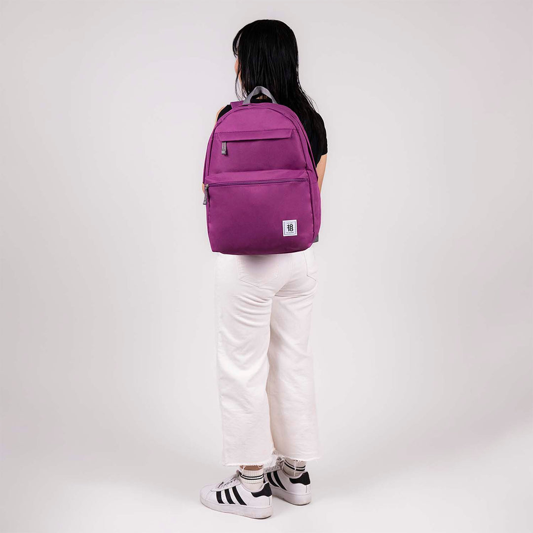 Mochila juvenil de color lila con detalles en gris y múltiples compartimentos frontales.