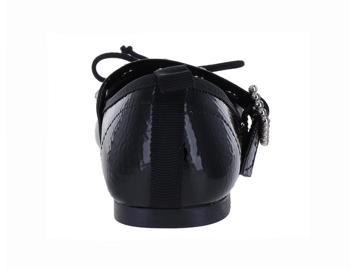Zapato plano de charol negro brillante con hebilla plateada y moño decorativo.