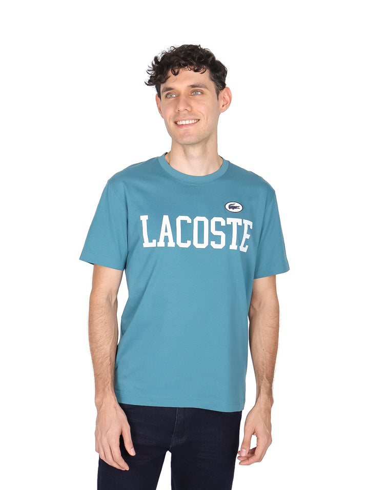 Hombre vistiendo una camiseta azul de manga corta con la palabra LACOSTE en blanco en el pecho.
