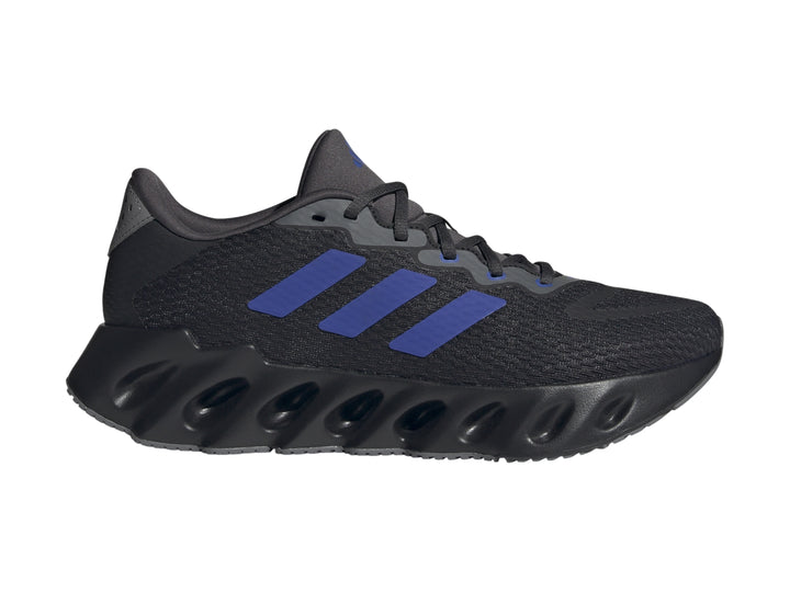 Tenis Adidas Switch Run color negro con tres franjas azules y suela ondulada para hombre.