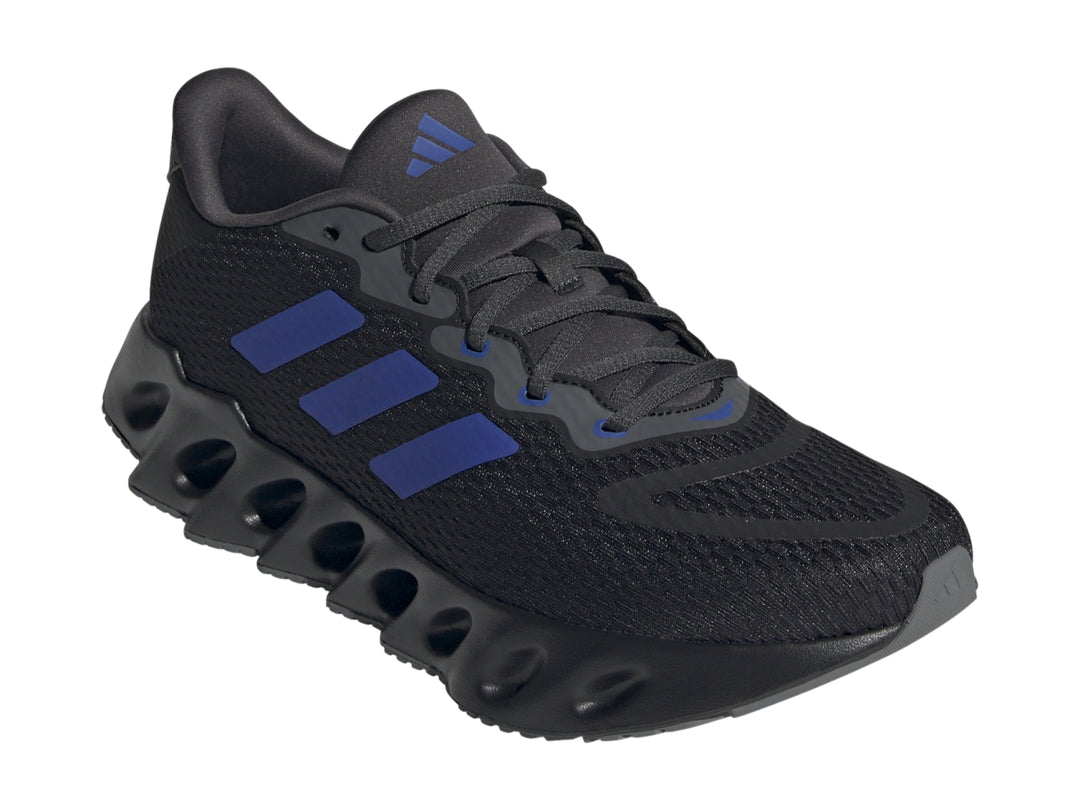 Tenis Adidas Switch Run color negro con tres franjas azules y suela ondulada para hombre.