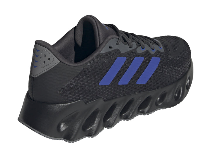 Tenis Adidas Switch Run color negro con tres franjas azules y suela ondulada para hombre.