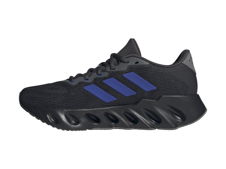 Tenis Adidas Switch Run color negro con tres franjas azules y suela ondulada para hombre.
