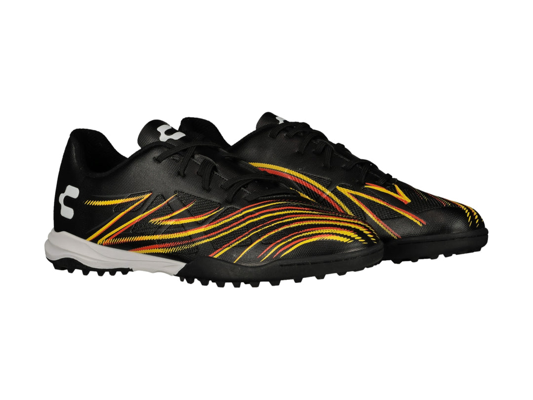 Zapato de fútbol Charly color negro con rayas amarillas y naranjas, suela blanca y negra para pasto sintético.