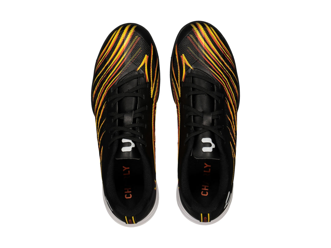 Zapato de fútbol Charly color negro con rayas amarillas y naranjas, suela blanca y negra para pasto sintético.