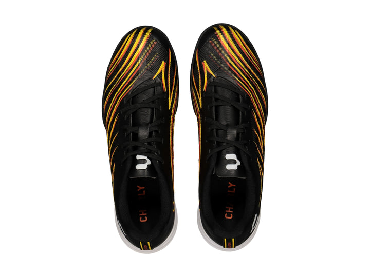 Zapato de fútbol Charly color negro con rayas amarillas y naranjas, suela blanca y negra para pasto sintético.