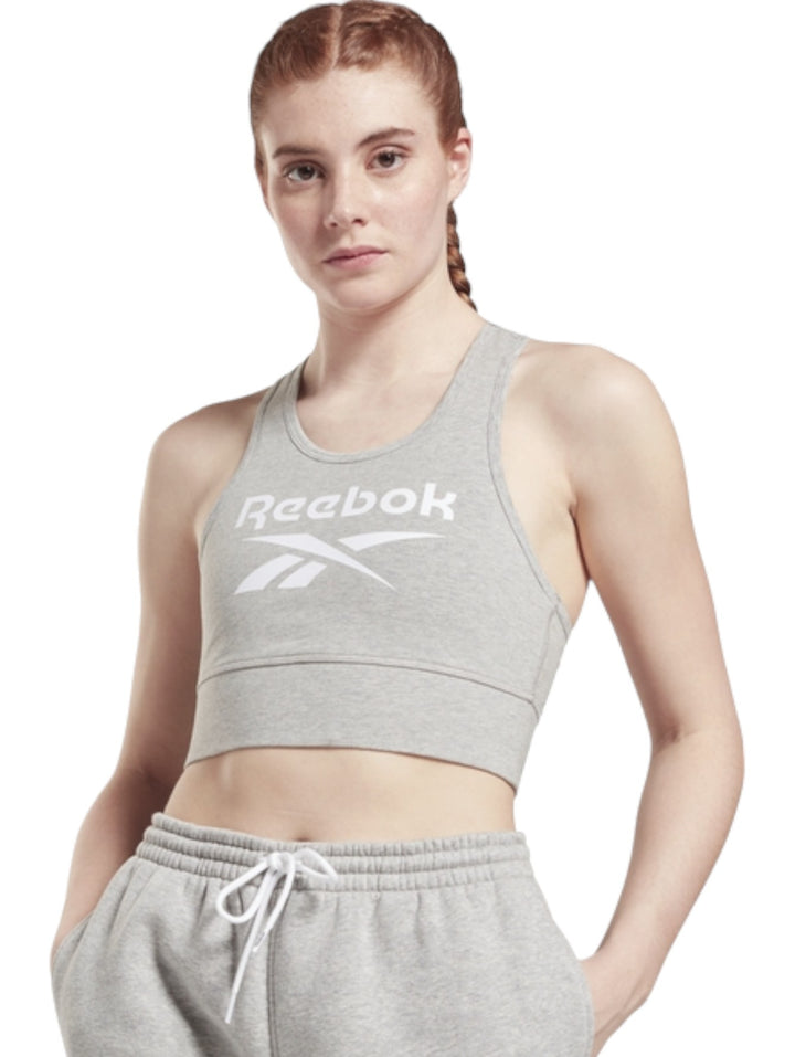 Mujer vistiendo un bralette deportivo gris de Reebok con logotipo blanco frontal y pantalones a juego.
