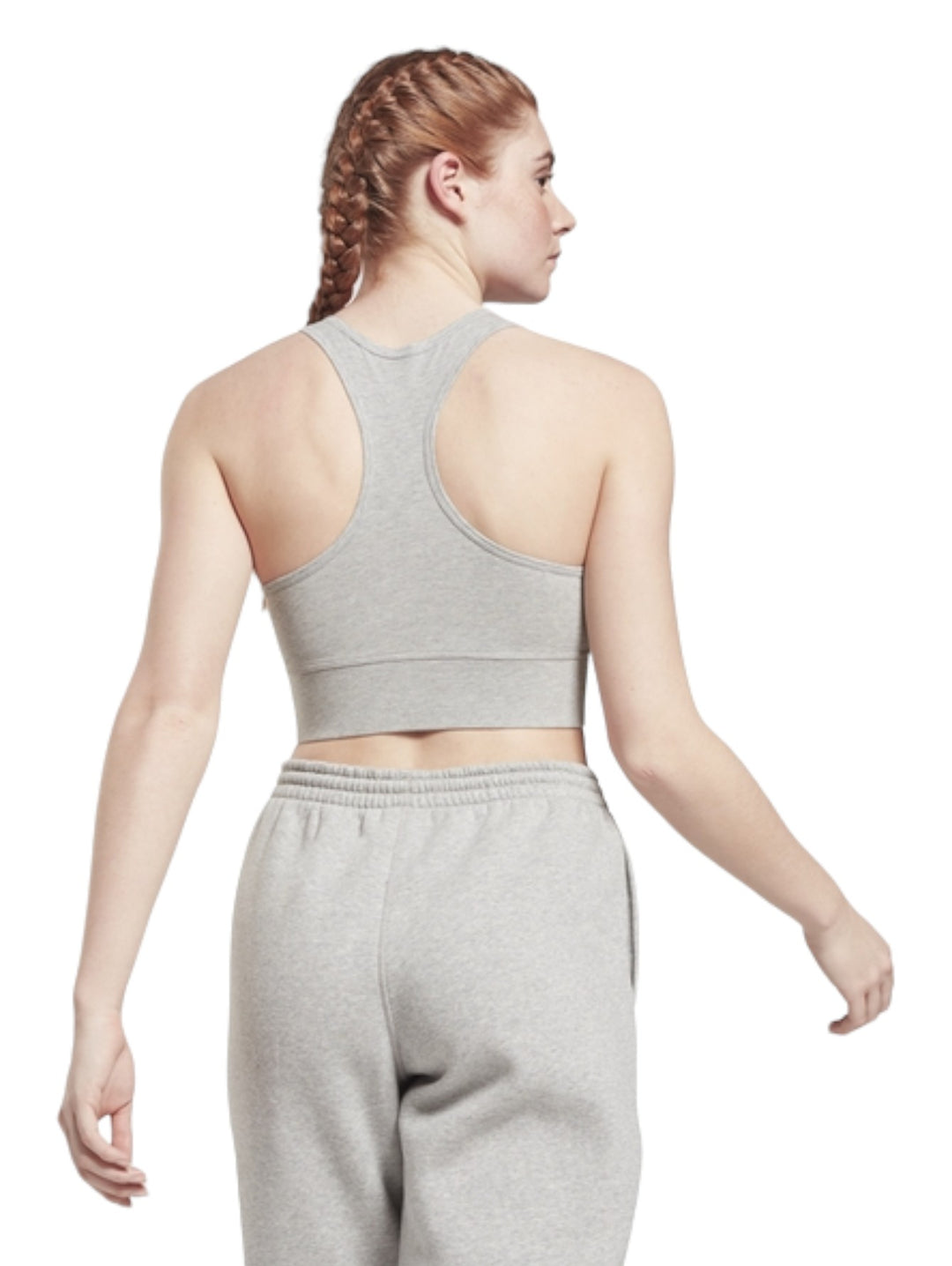 Mujer vistiendo un bralette deportivo gris de Reebok con logotipo blanco frontal y pantalones a juego.