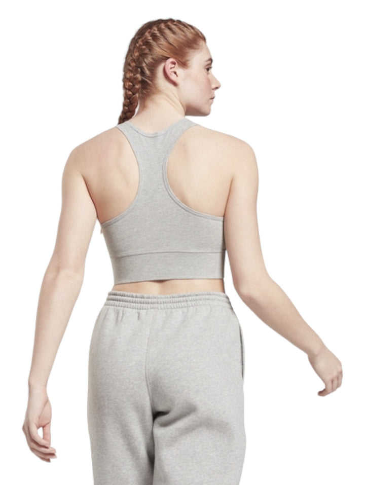 Mujer vistiendo un bralette deportivo gris de Reebok con logotipo blanco frontal y pantalones a juego.