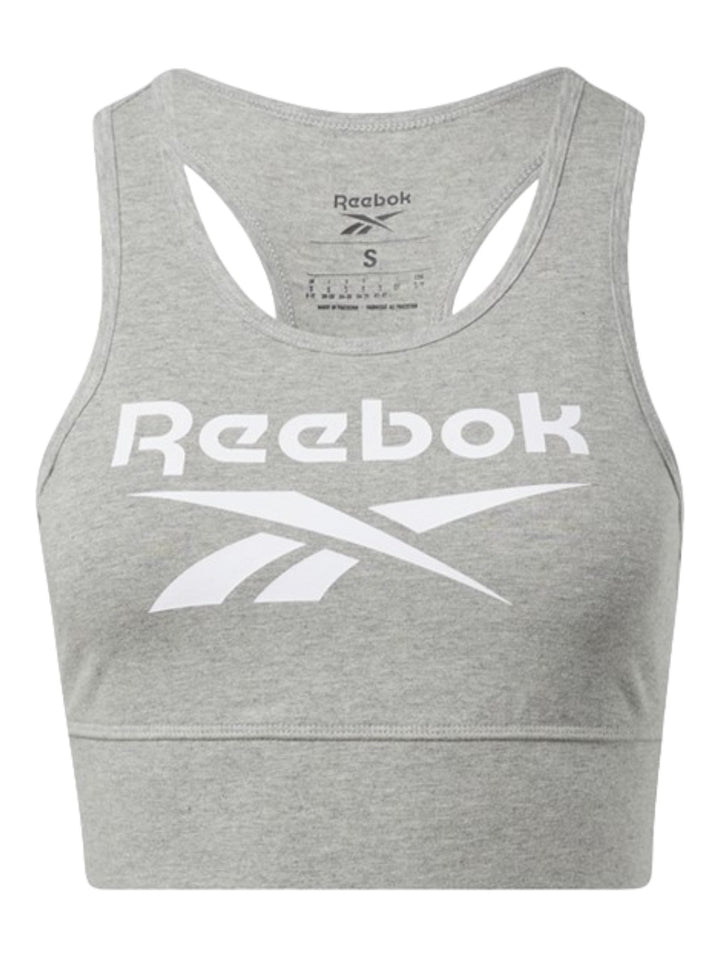 Mujer vistiendo un bralette deportivo gris de Reebok con logotipo blanco frontal y pantalones a juego.