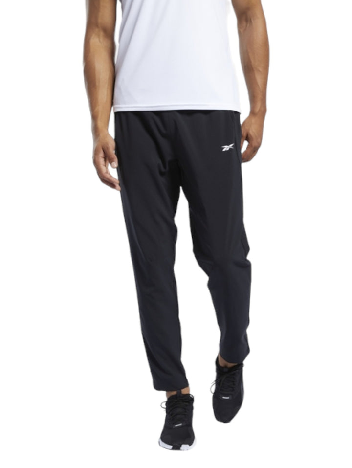 Hombre vistiendo pantalones deportivos Reebok de color negro, corte recto y diseño ligero para entrenamiento.