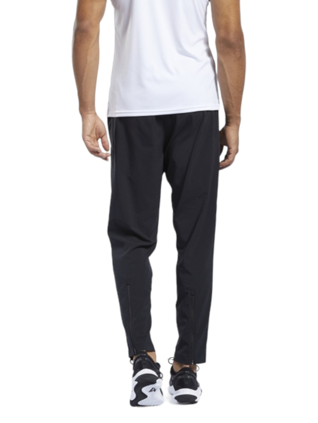 Hombre vistiendo pantalones deportivos Reebok de color negro, corte recto y diseño ligero para entrenamiento.