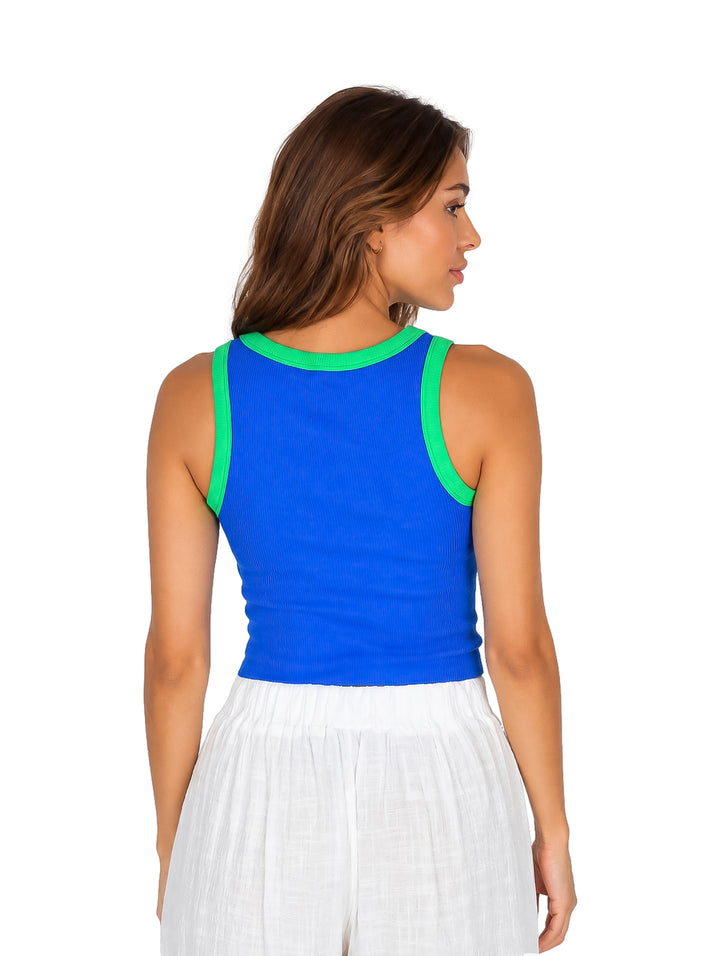 Mujer vistiendo un top básico azul sin mangas con ribete verde y pantalones blancos.