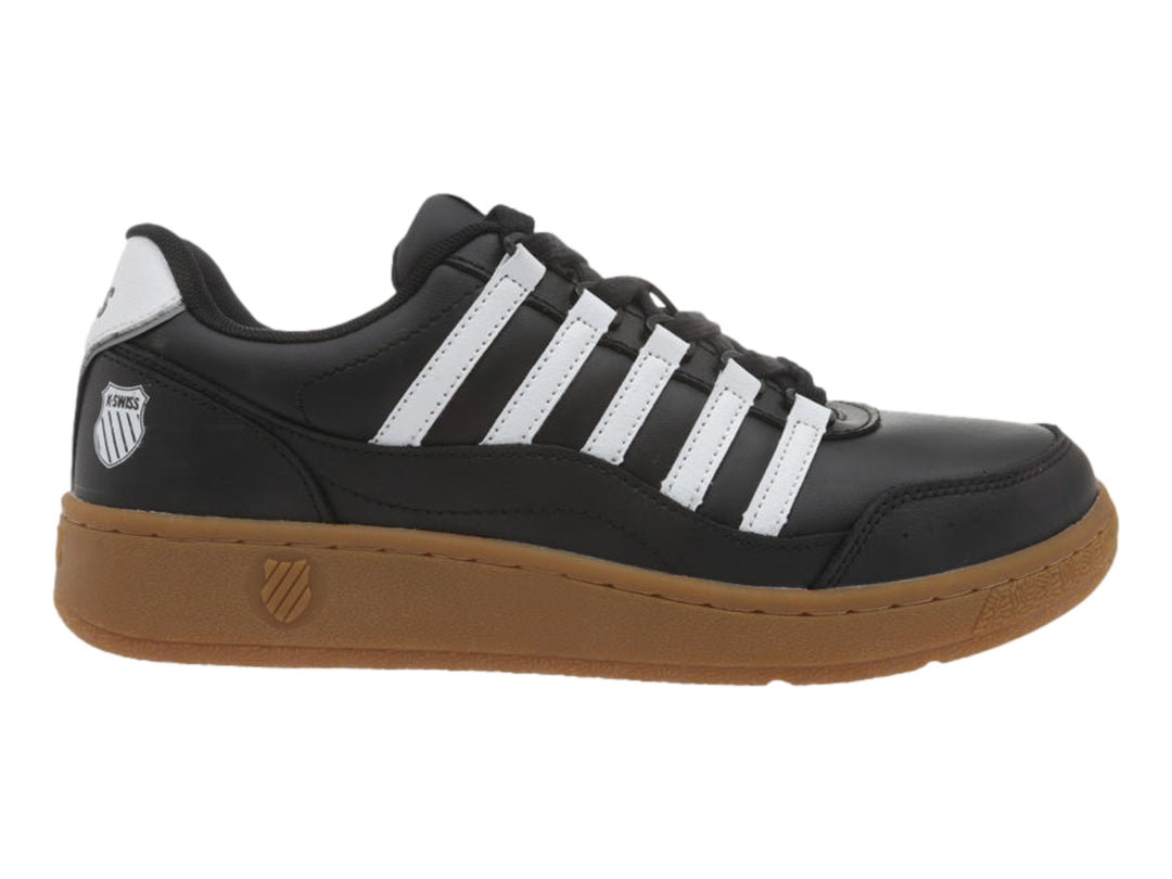 Tenis K-Swiss color negro con rayas blancas y suela de goma color marrón.