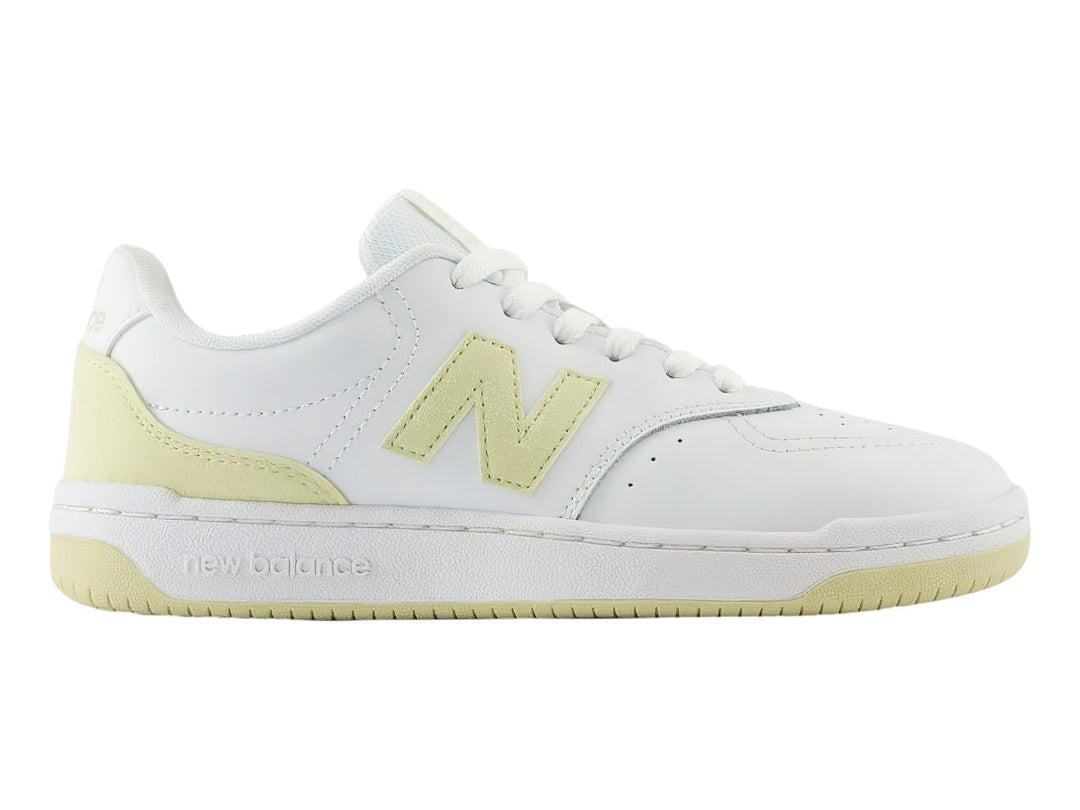 Tenis New Balance color blanco con detalles en amarillo, diseño deportivo de corte bajo.