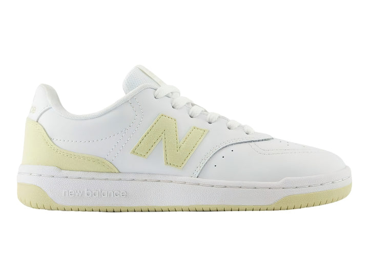 Tenis New Balance color blanco con detalles en amarillo, diseño deportivo de corte bajo.