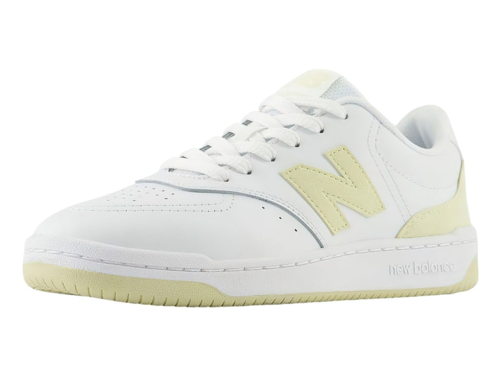 Tenis New Balance color blanco con detalles en amarillo, diseño deportivo de corte bajo.