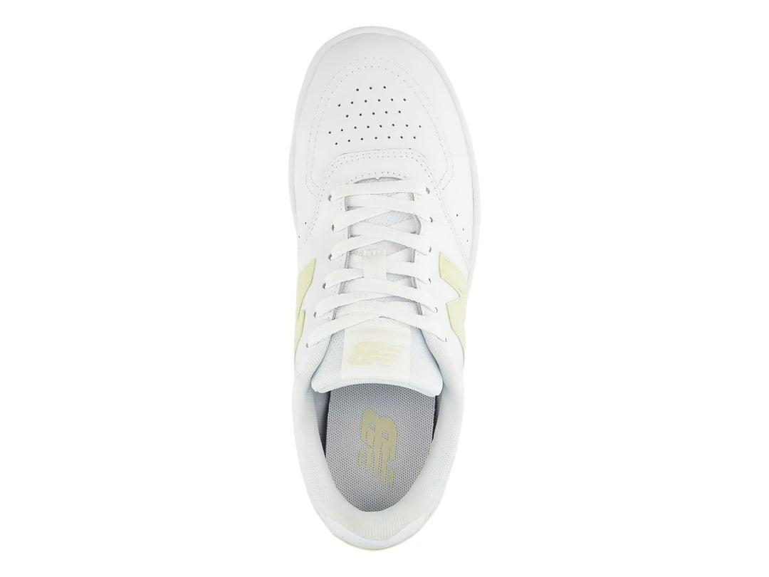 Tenis New Balance color blanco con detalles en amarillo, diseño deportivo de corte bajo.