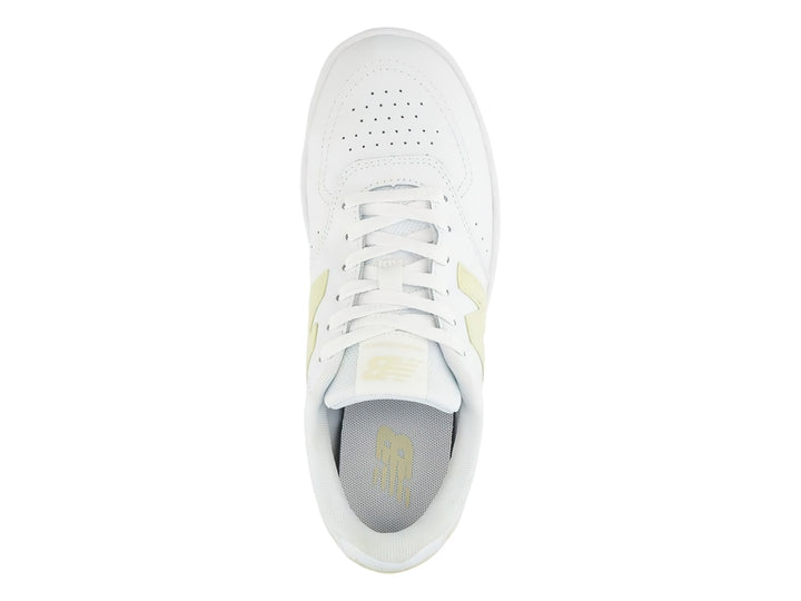 Tenis New Balance color blanco con detalles en amarillo, diseño deportivo de corte bajo.