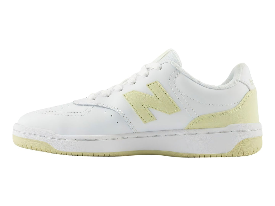 Tenis New Balance color blanco con detalles en amarillo, diseño deportivo de corte bajo.