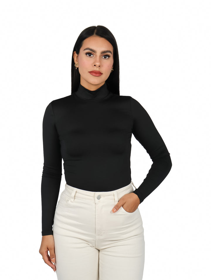 Mujer vistiendo un body negro de manga larga y cuello alto con pantalones blancos.