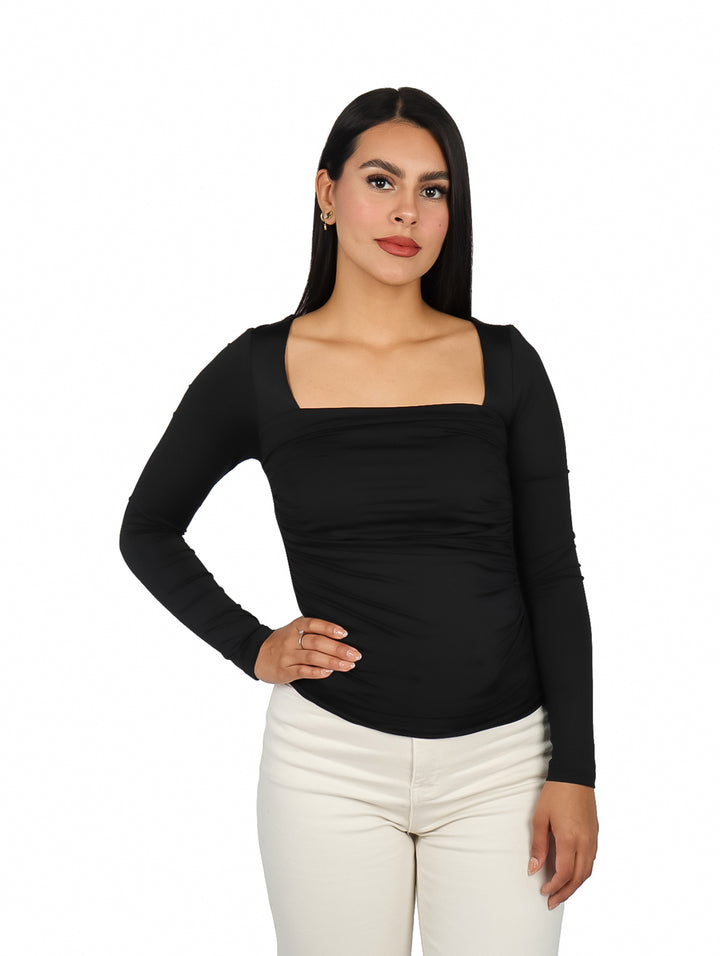 Mujer vistiendo blusa negra de manga larga con escote cuadrado y pantalones blancos.