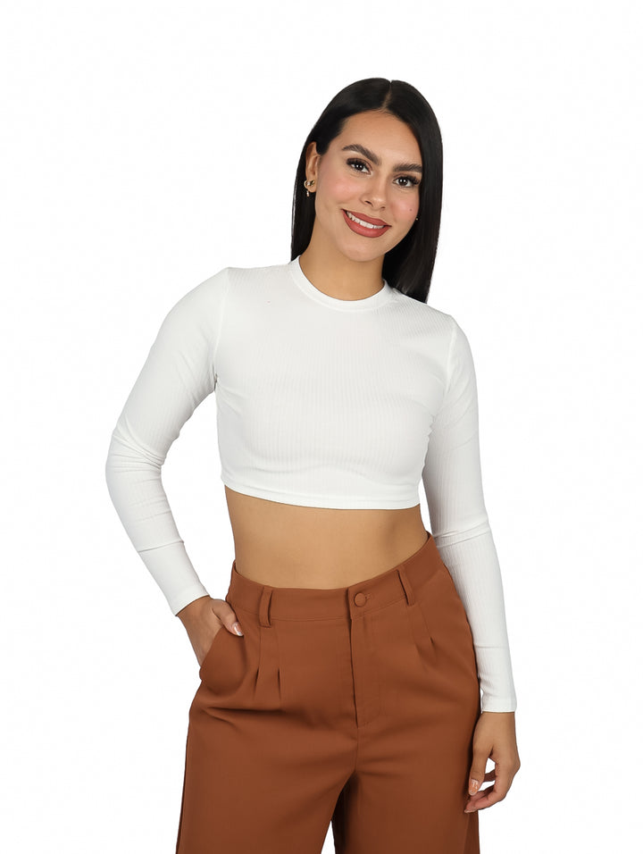 Mujer vistiendo un top corto color ivory de manga larga y pantalones marrones.