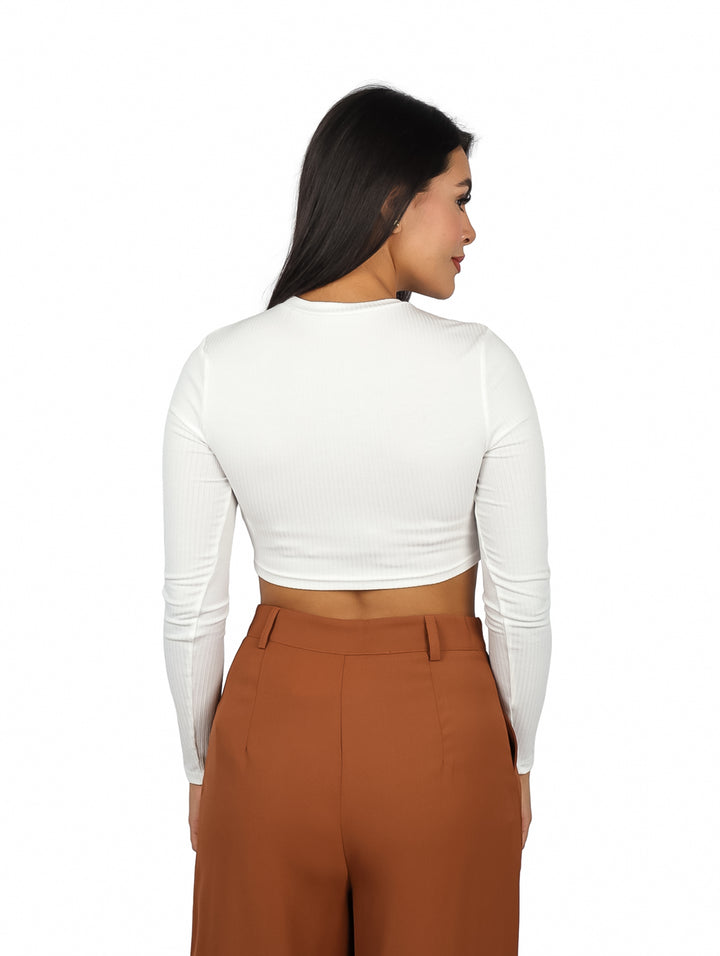 Mujer vistiendo un top corto color ivory de manga larga y pantalones marrones.