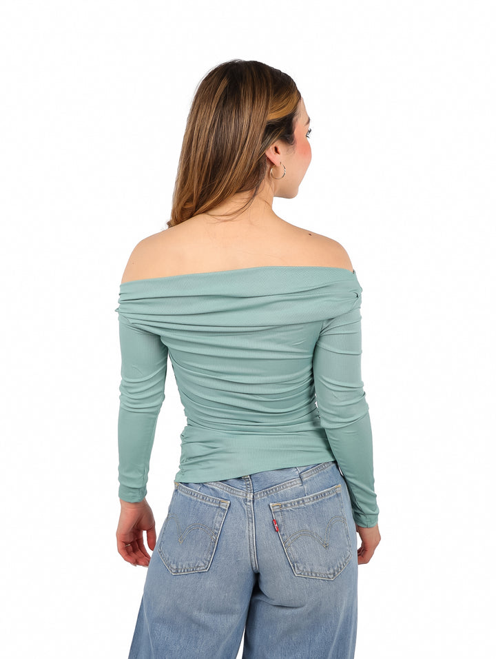 Mujer vistiendo blusa color jade de un solo hombro y pantalones azules.