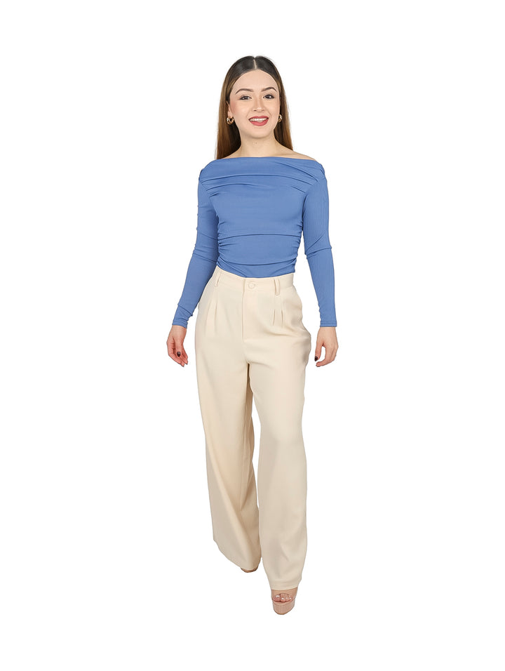 Mujer vistiendo blusa azul royal ajustada con cuello off-the-shoulder y pantalones color crema.