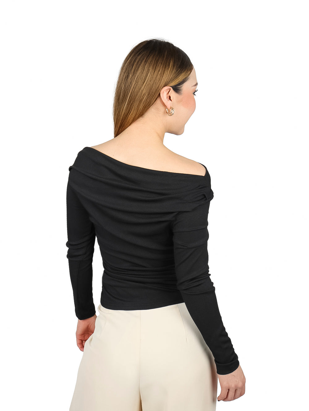 Mujer vistiendo blusa negra de manga larga con hombros descubiertos y pantalones color crema.