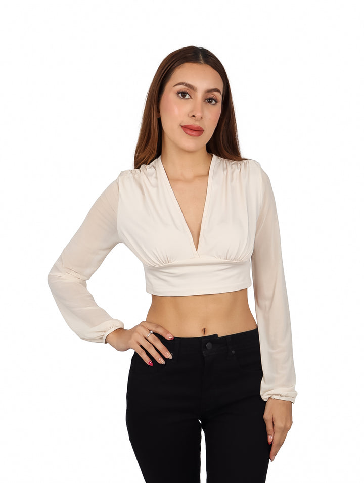 Mujer vistiendo blusa corta color arena con escote en V y manga larga, combinada con pantalones negros.