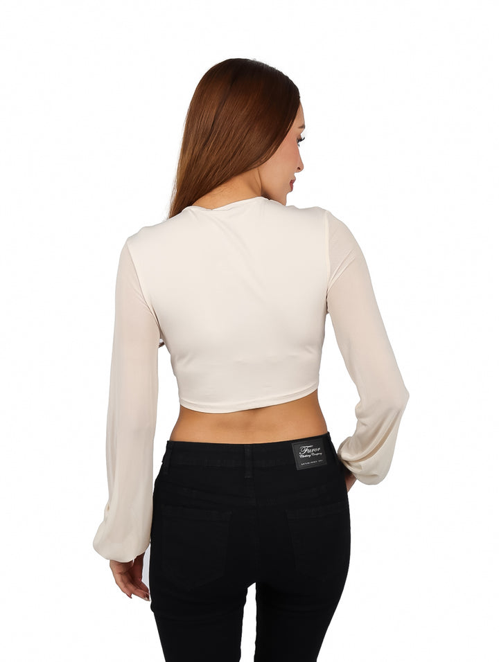 Mujer vistiendo blusa corta color arena con escote en V y manga larga, combinada con pantalones negros.