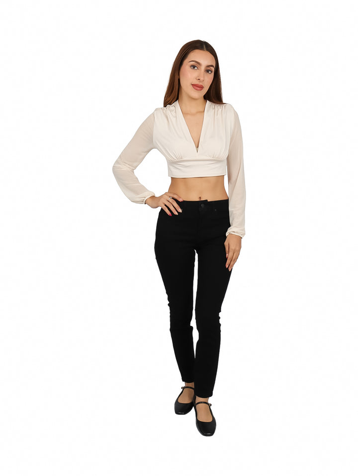 Mujer vistiendo blusa corta color arena con escote en V y manga larga, combinada con pantalones negros.