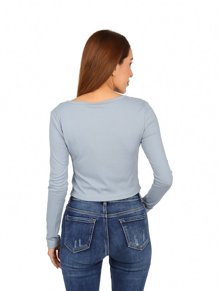 Mujer vistiendo blusa corta azul claro con botones frontales y manga larga.