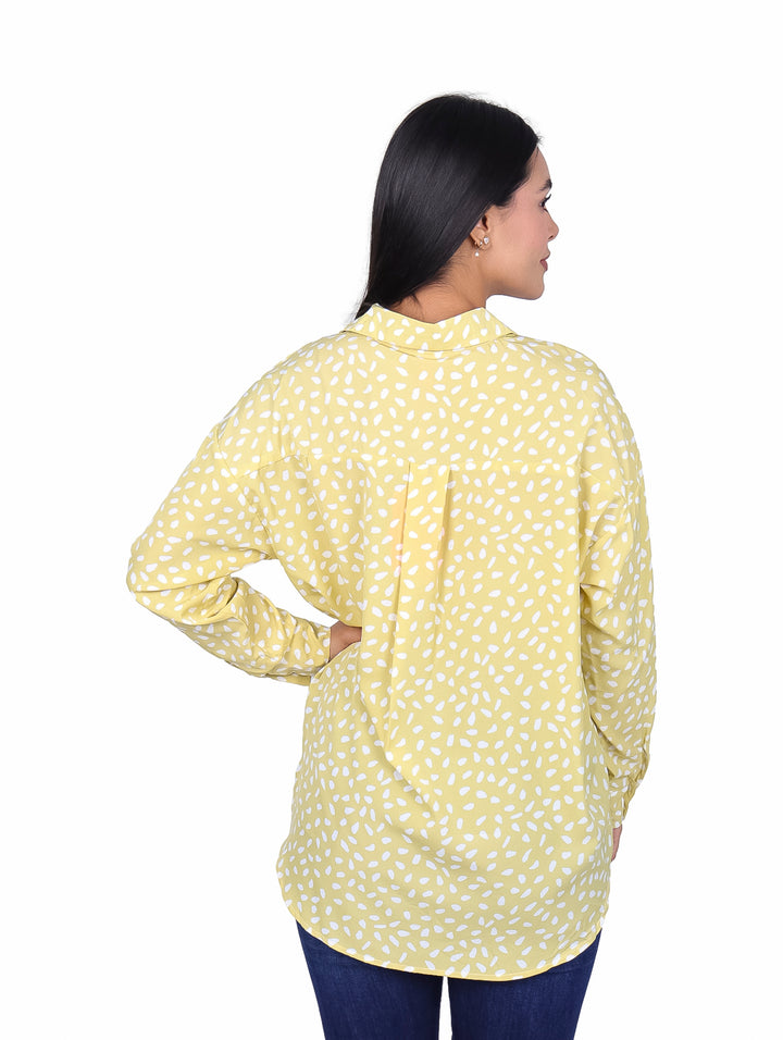 Mujer vistiendo una camisa de manga larga color lima con estampado de pequeños óvalos blancos.