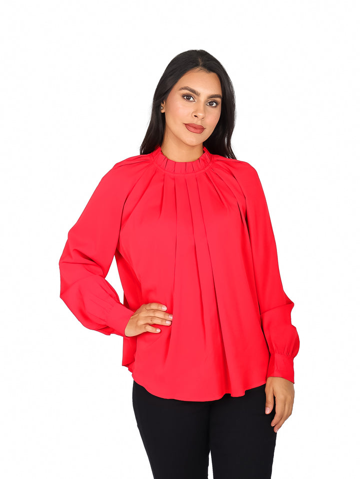 Mujer vistiendo blusa roja de cuello alto con pliegues frontales y mangas largas.
