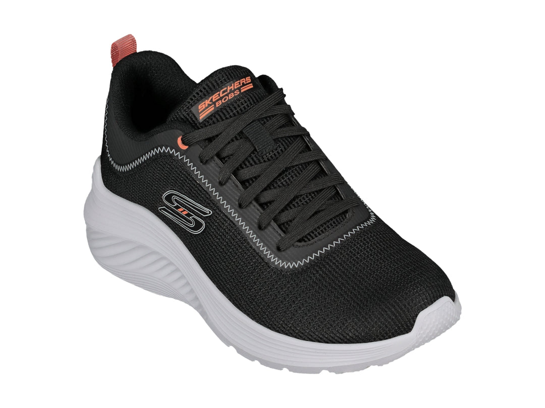Tenis deportivos Skechers color negro con suela blanca y detalle naranja en el talón.